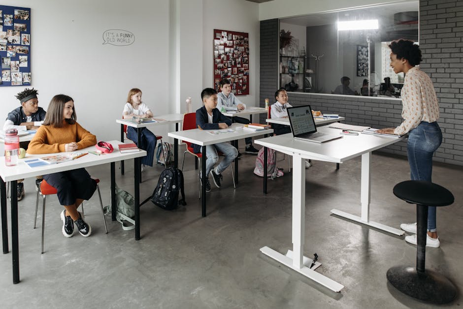 A diverse group of students attentively listens to a teacher in a modern classroom setting.